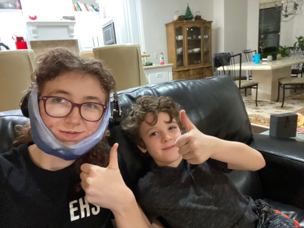 Trinity and her brother give a thumbs up while trinity has a cold press on her face